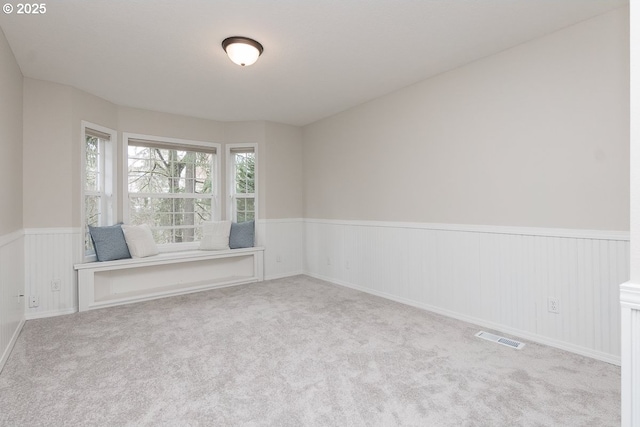 carpeted spare room featuring visible vents and a wainscoted wall