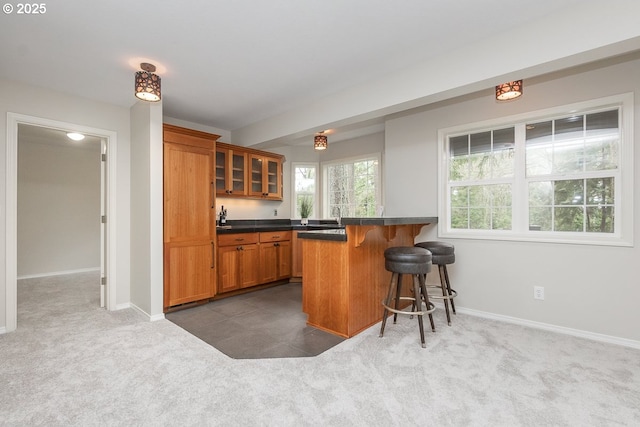 kitchen featuring dark countertops, glass insert cabinets, dark carpet, a breakfast bar area, and brown cabinets