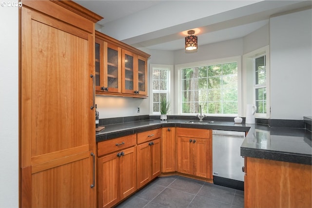 kitchen featuring brown cabinetry, a sink, glass insert cabinets, stainless steel dishwasher, and dark tile patterned floors