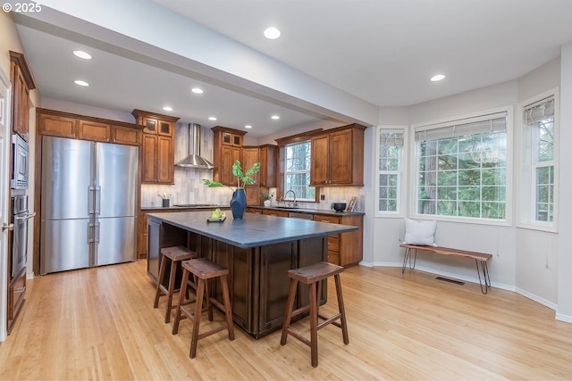 kitchen featuring dark countertops, tasteful backsplash, wall chimney range hood, a kitchen breakfast bar, and stainless steel appliances