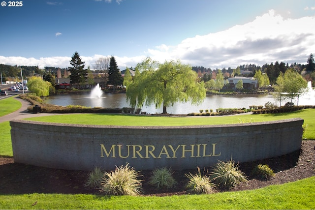 community / neighborhood sign featuring a water view and a lawn