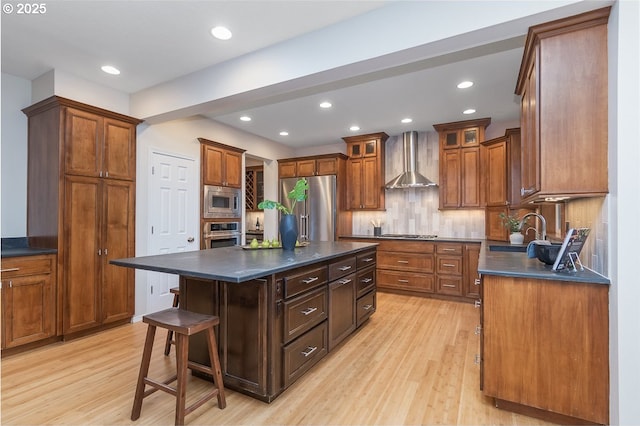 kitchen featuring a kitchen island, a sink, appliances with stainless steel finishes, dark countertops, and wall chimney range hood