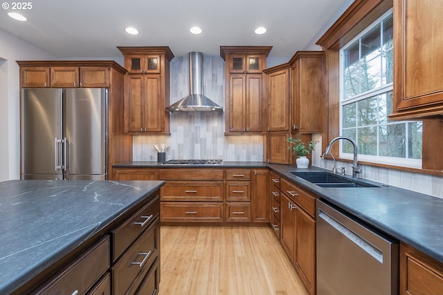 kitchen with a sink, stainless steel appliances, dark countertops, and wall chimney exhaust hood