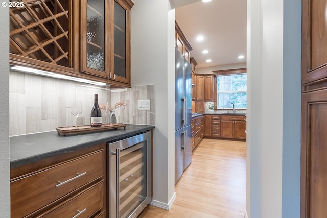 bar featuring light wood-type flooring, high end fridge, wine cooler, a bar, and decorative backsplash