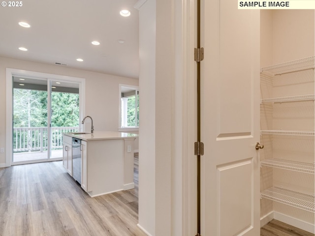 kitchen with sink, light wood-type flooring, stainless steel dishwasher, a kitchen island with sink, and white cabinets