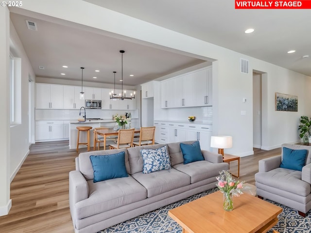 living room with visible vents, light wood finished floors, baseboards, and an inviting chandelier