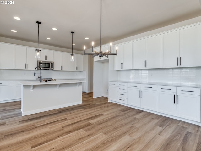 kitchen featuring decorative backsplash, light countertops, stainless steel microwave, light wood-style floors, and recessed lighting