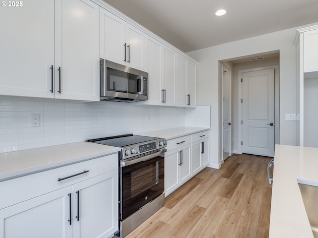 kitchen with light countertops, stainless steel appliances, white cabinets, and light wood-style flooring