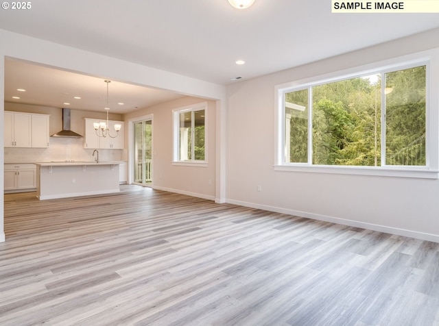 unfurnished living room featuring light hardwood / wood-style flooring, a notable chandelier, plenty of natural light, and sink