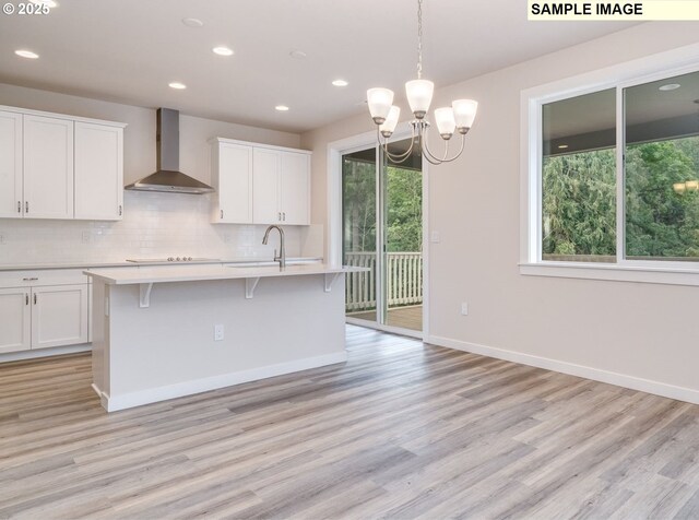 kitchen featuring an island with sink, white cabinets, and wall chimney exhaust hood