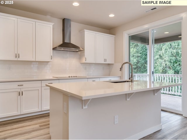 kitchen with wall chimney exhaust hood, sink, a center island with sink, and white cabinets