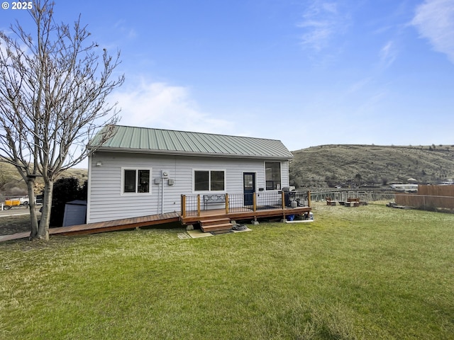 rear view of house with metal roof, a deck with mountain view, a lawn, and fence