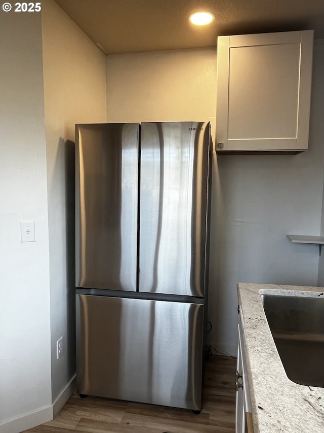 kitchen featuring freestanding refrigerator, white cabinetry, a sink, wood finished floors, and baseboards