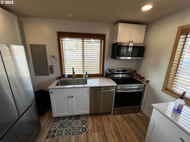 kitchen featuring appliances with stainless steel finishes, light stone counters, light wood-type flooring, white cabinetry, and a sink