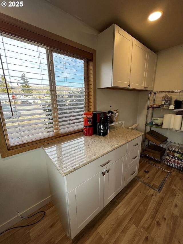 kitchen with light stone countertops, light wood-style floors, baseboards, and white cabinets