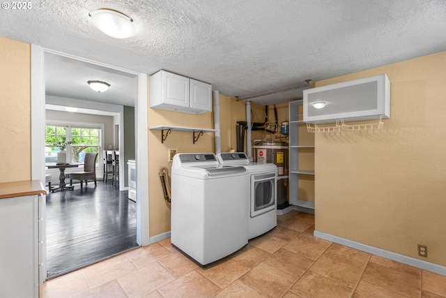 laundry area featuring a textured ceiling, cabinet space, baseboards, water heater, and washer and clothes dryer
