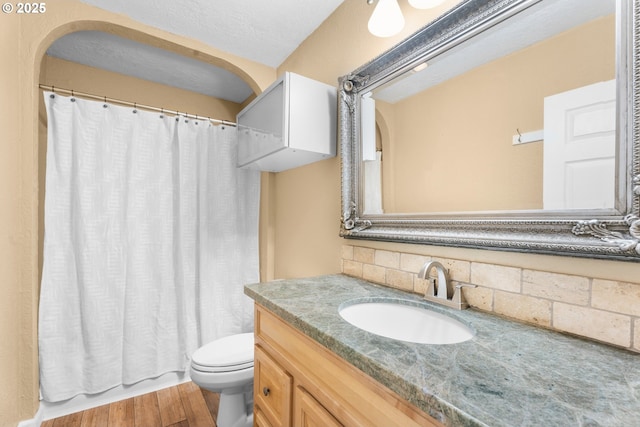 bathroom featuring vanity, decorative backsplash, wood finished floors, curtained shower, and toilet