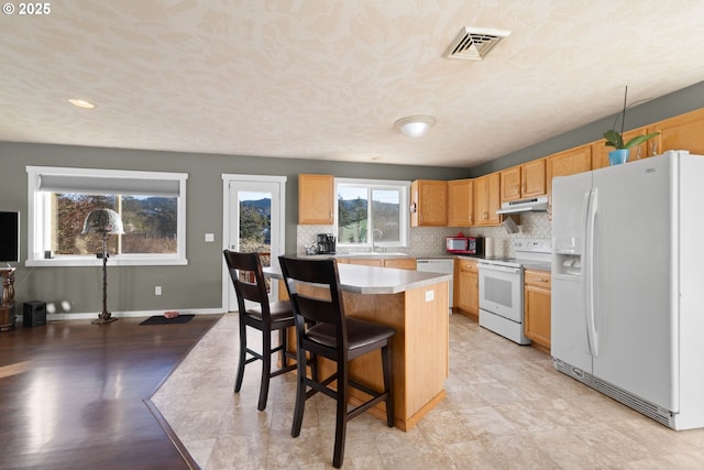 kitchen featuring white appliances, a kitchen island, tasteful backsplash, sink, and a breakfast bar area