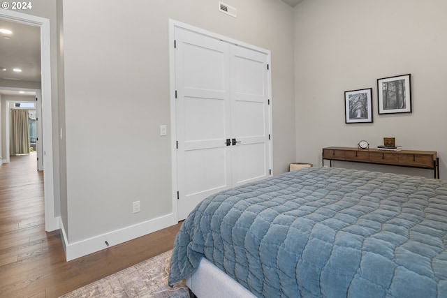 bedroom with a closet, wood finished floors, visible vents, and baseboards