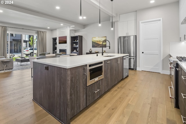 kitchen with dark brown cabinetry, high quality appliances, white cabinets, light countertops, and an island with sink