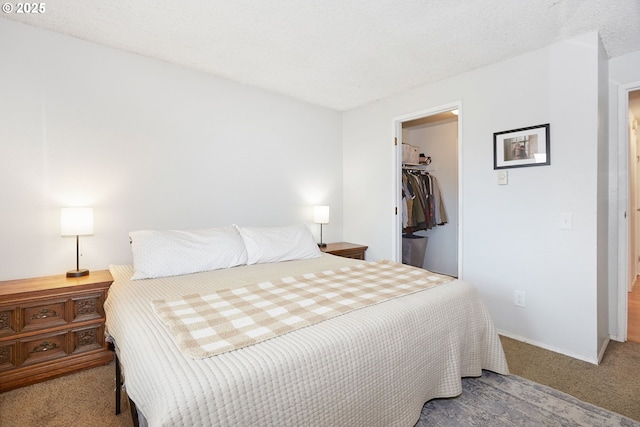 carpeted bedroom with a closet, a textured ceiling, a walk in closet, and baseboards