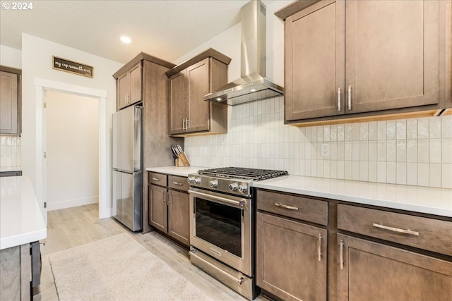 kitchen with decorative backsplash, light hardwood / wood-style flooring, wall chimney range hood, and appliances with stainless steel finishes