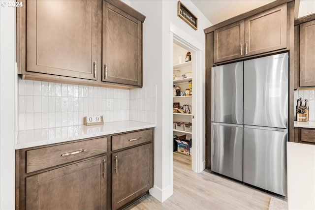 kitchen featuring decorative backsplash, stainless steel fridge, dark brown cabinetry, and light hardwood / wood-style floors