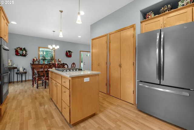 kitchen with light brown cabinetry, a kitchen island, decorative light fixtures, and appliances with stainless steel finishes