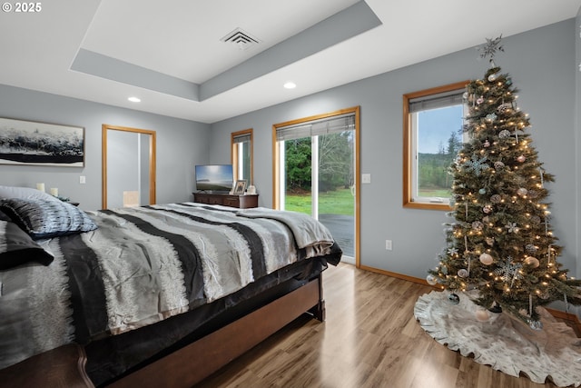 bedroom featuring a raised ceiling, light hardwood / wood-style flooring, and access to outside