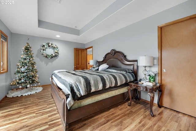 bedroom with light wood-type flooring and a tray ceiling