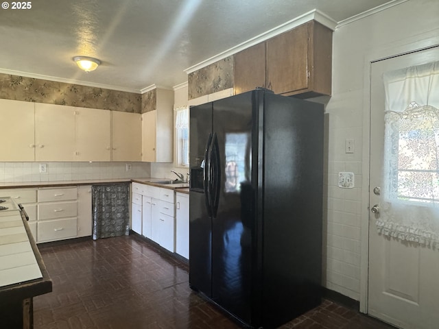 kitchen featuring tile counters, backsplash, crown molding, black fridge, and a sink