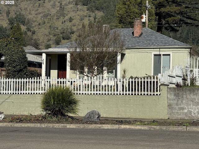 view of front facade featuring a fenced front yard, a chimney, and roof with shingles