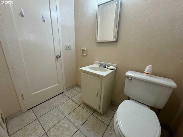 half bath featuring a textured wall, vanity, tile patterned flooring, and toilet