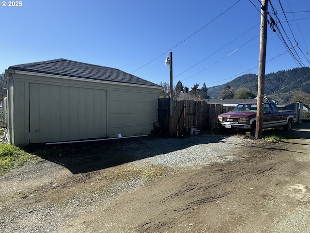 exterior space featuring a mountain view, an outdoor structure, fence, driveway, and roof with shingles