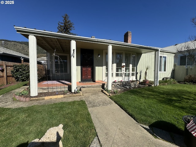 view of front of house with a chimney, fence, a porch, and a front yard