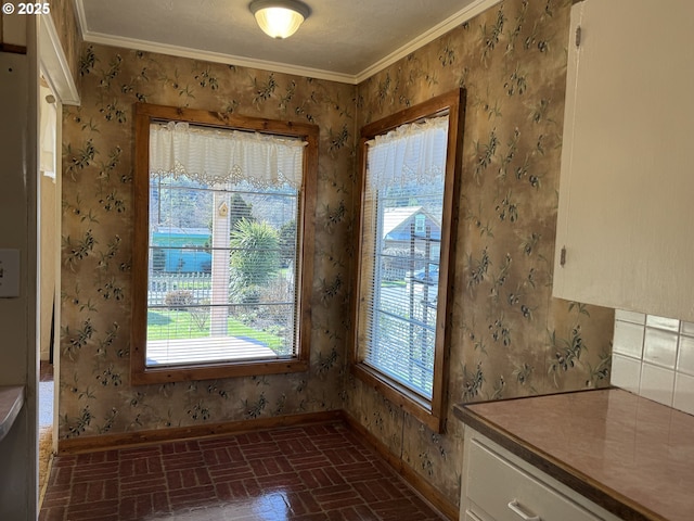 unfurnished dining area featuring baseboards, crown molding, brick floor, and wallpapered walls