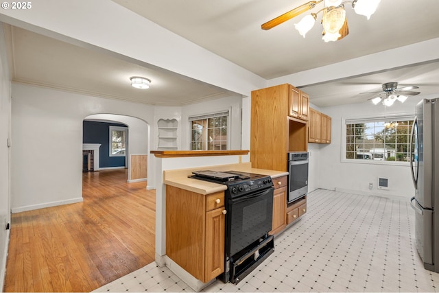 kitchen featuring arched walkways, appliances with stainless steel finishes, a ceiling fan, and light countertops