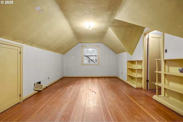 additional living space featuring baseboards, a textured ceiling, lofted ceiling, and wood-type flooring