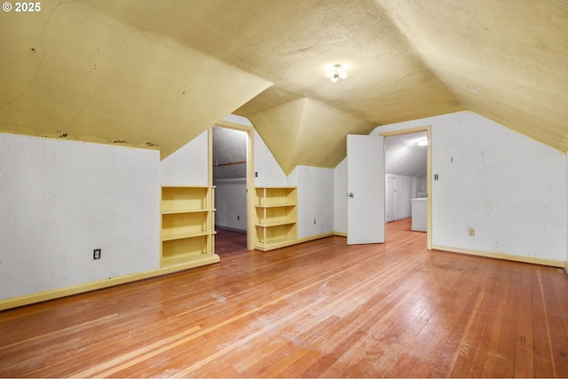 additional living space featuring baseboards, a textured ceiling, lofted ceiling, and wood-type flooring