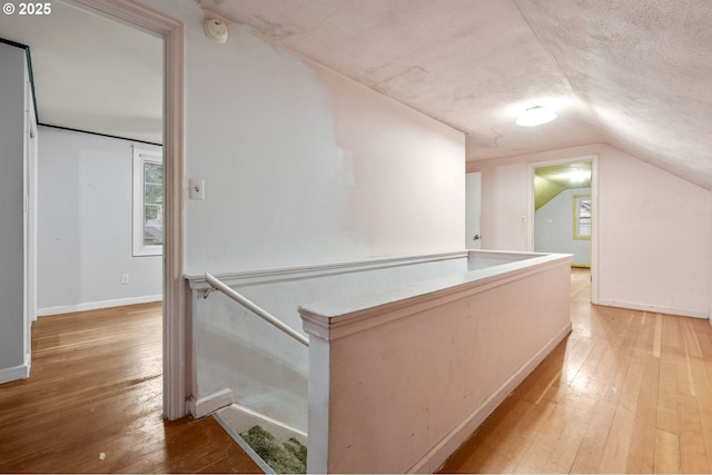 hallway with hardwood / wood-style floors, vaulted ceiling, an upstairs landing, and baseboards