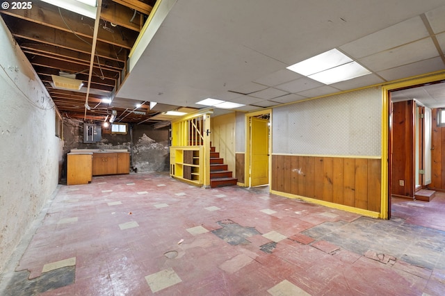 basement featuring wallpapered walls, a wainscoted wall, electric panel, and stairway