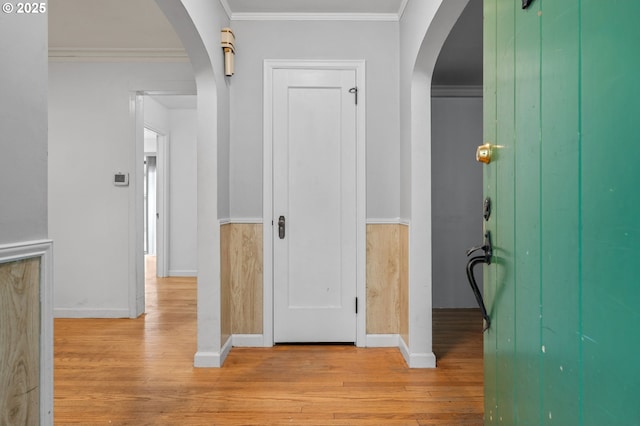 hall featuring arched walkways, light wood-style flooring, crown molding, and baseboards