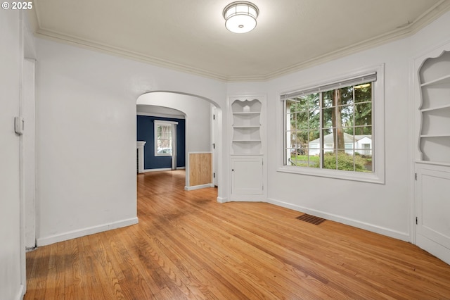 spare room with light wood finished floors, visible vents, built in shelves, baseboards, and arched walkways