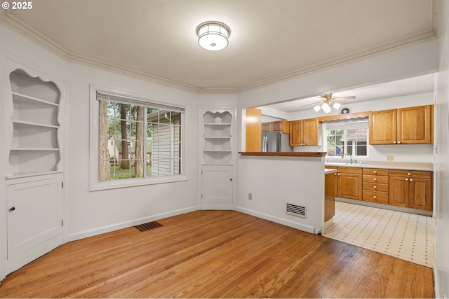 kitchen featuring visible vents, freestanding refrigerator, light wood-style floors, brown cabinetry, and crown molding