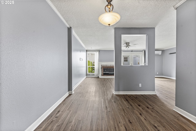hallway featuring baseboards, an AC wall unit, a textured wall, crown molding, and wood finished floors