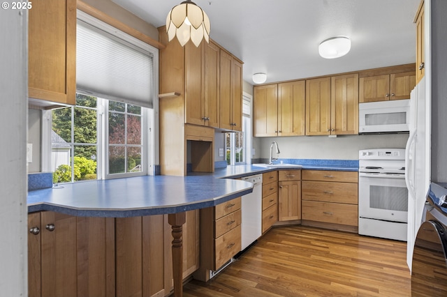 kitchen featuring white appliances, a sink, a peninsula, and wood finished floors