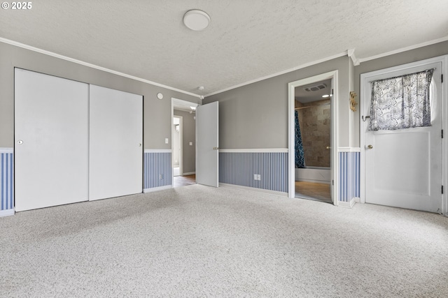 unfurnished bedroom with a closet, ornamental molding, a textured ceiling, a wainscoted wall, and visible vents