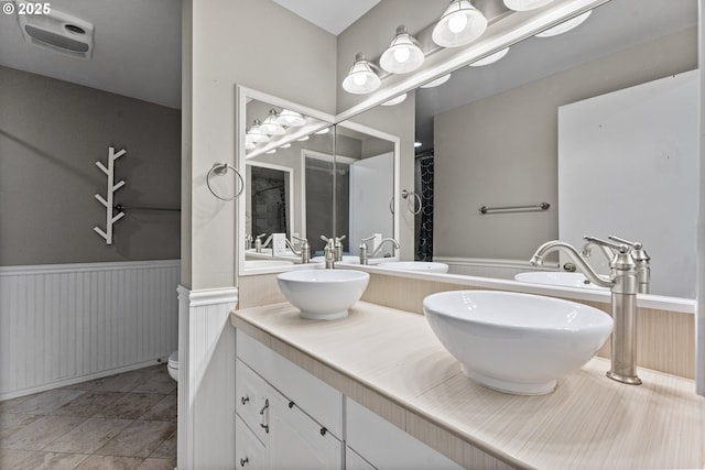 full bath featuring double vanity, wainscoting, a sink, and toilet