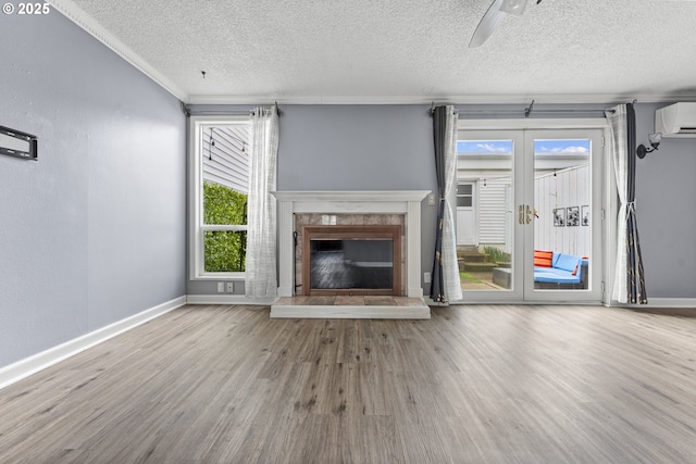 unfurnished living room featuring crown molding, a glass covered fireplace, wood finished floors, a wall mounted air conditioner, and baseboards