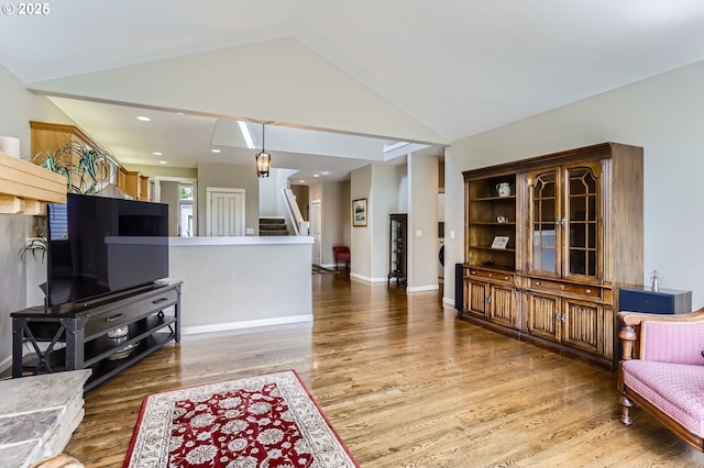 living area featuring stairs, wood finished floors, vaulted ceiling, and baseboards